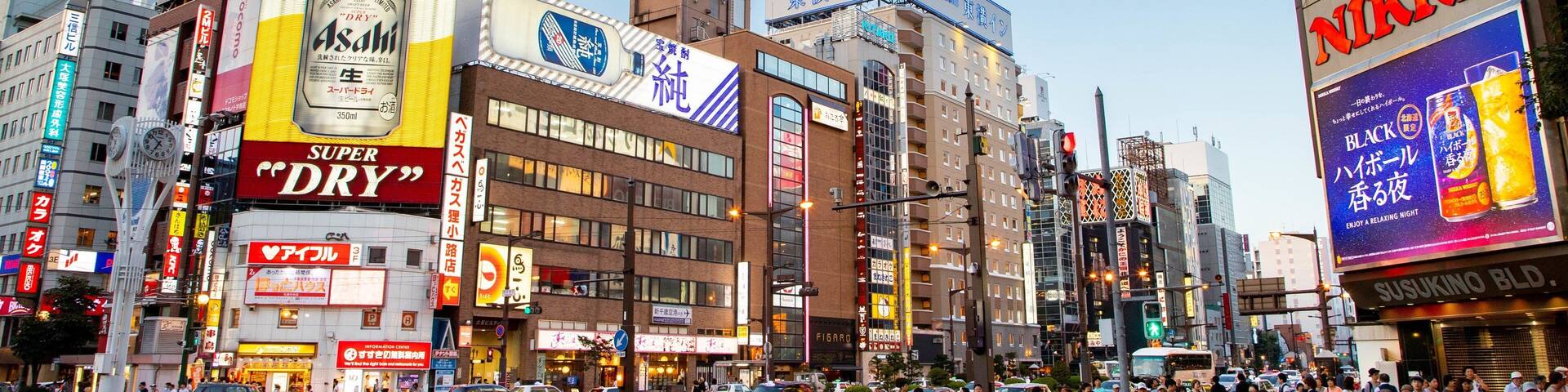 A busy urban street with various commercial buildings, including a prominent 'Nikko' sign and a 'Super Dry' beer advertisement.