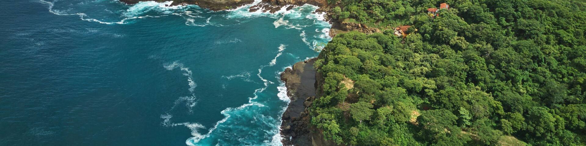 A coastal landscape with lush green hills, rocky cliffs, and a beach.