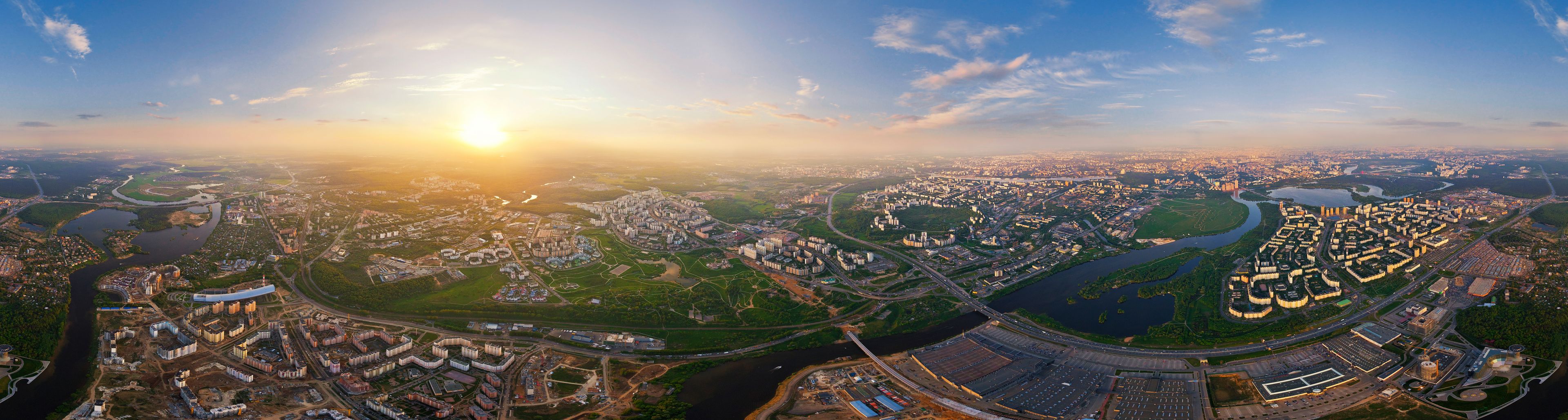 An aerial view of a city with a river, green spaces, and a large stadium.