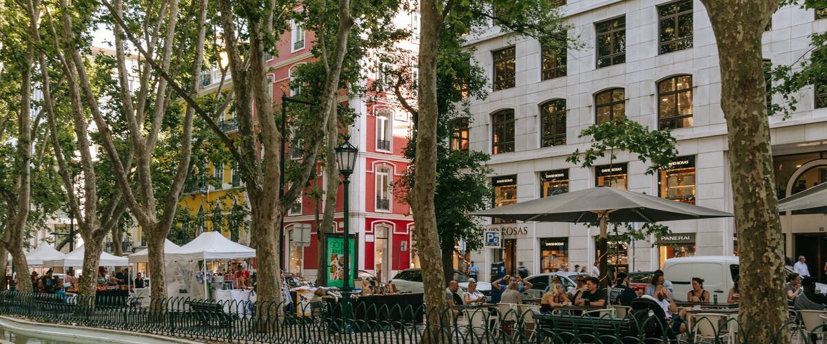 A riverside promenade with cafes, trees, and buildings.