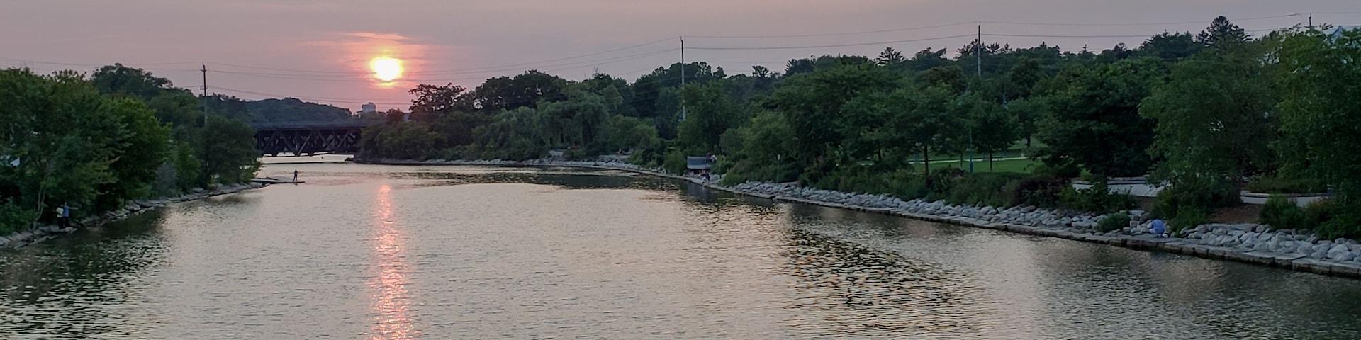 A river with a bridge in the distance, surrounded by trees and a clear sky.