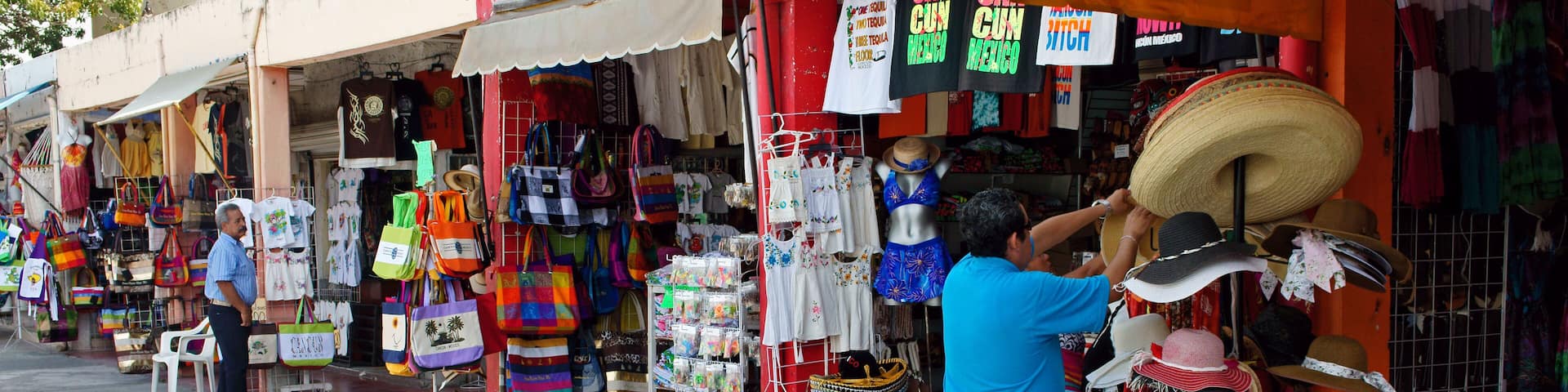 A street market with colorful bags, hats, and clothing stalls.