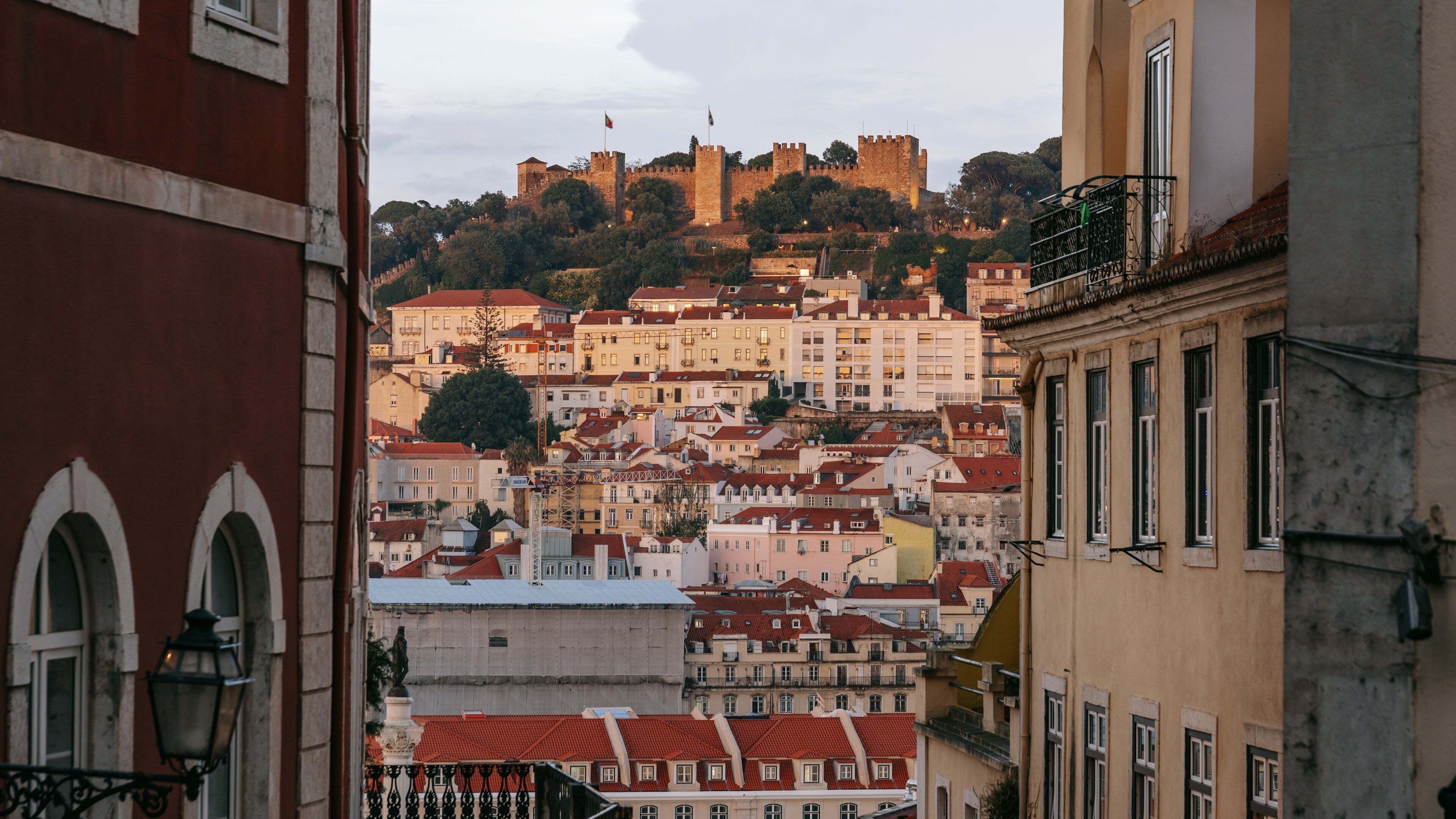 A cityscape with a prominent castle on a hill, surrounded by buildings with red-tiled roofs.