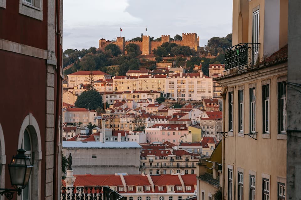 A cityscape with a prominent castle on a hill, surrounded by buildings with red-tiled roofs.