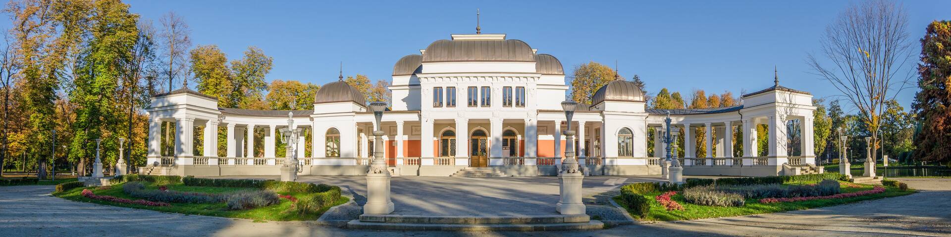 A large white building with a central dome and smaller domes on either side, surrounded by trees and a well-maintained garden.