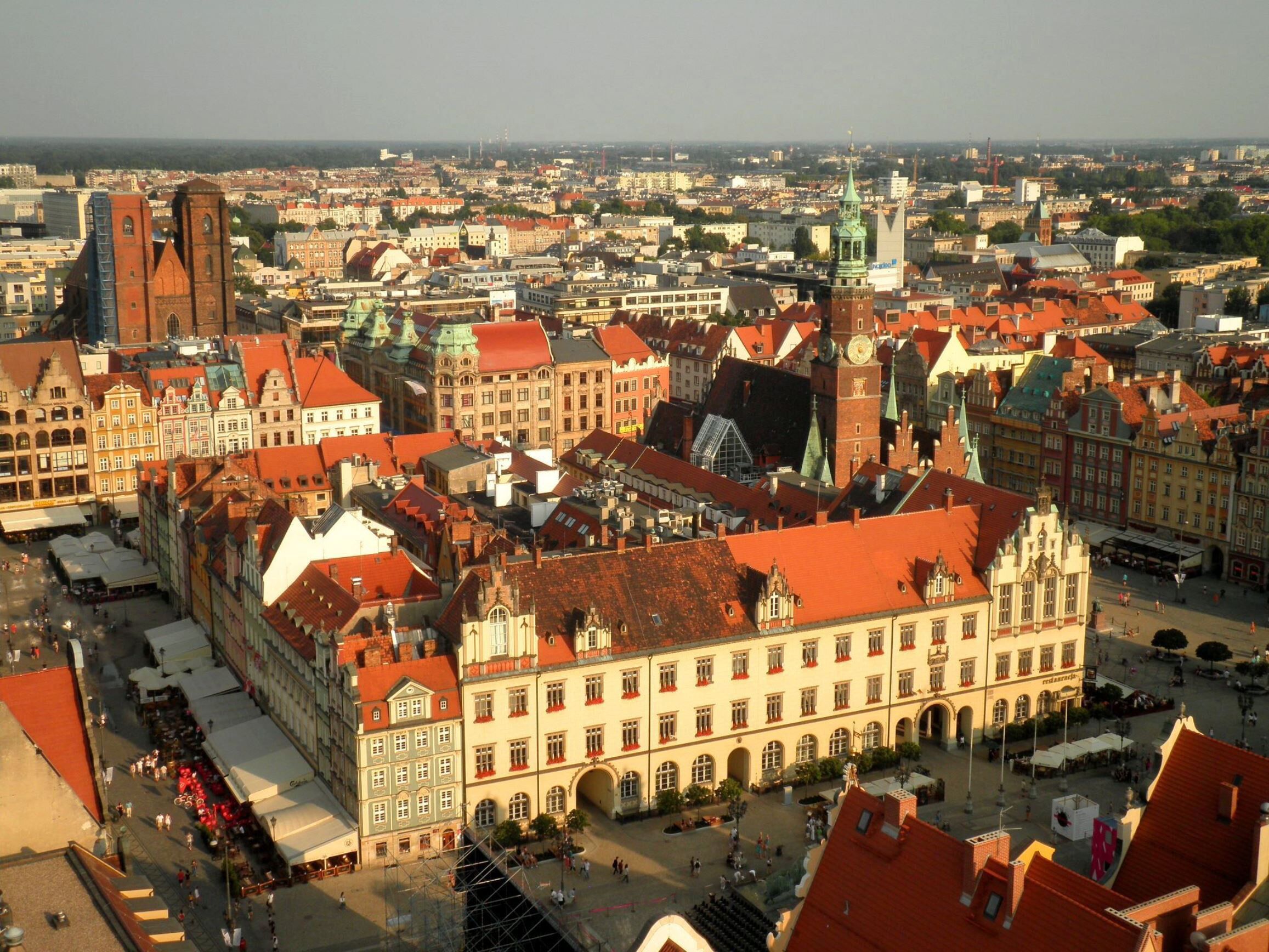 A historic European cityscape with prominent red-roofed buildings, a large church, and a green-domed tower.