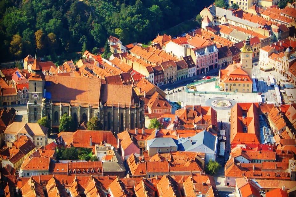 An aerial view of a historic town with red-roofed buildings, a prominent church, and a castle in the background.