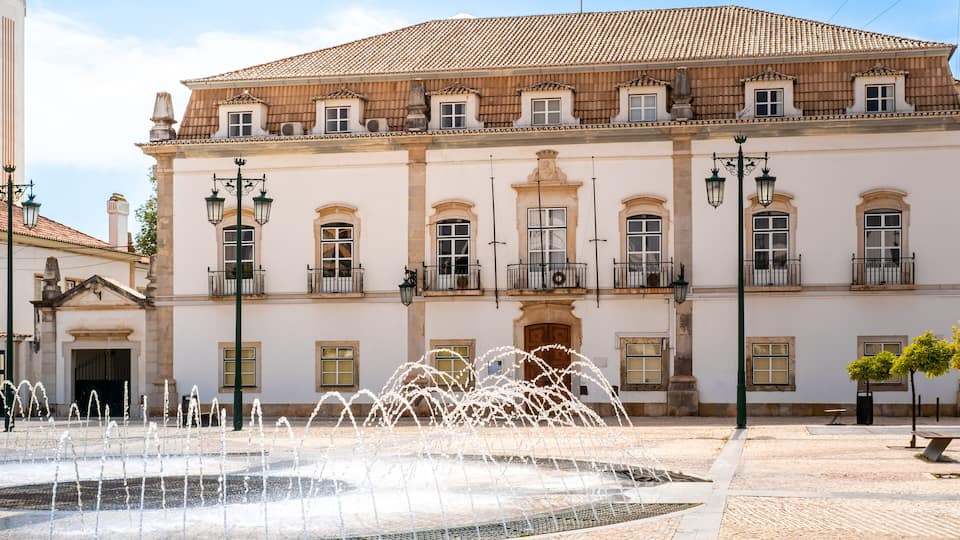 On a sunny spring day in May, the round water fountain on Praça 1 de Maio square stands in front of the impressive Portimão City Hall, providing a serene and tranquil backdrop to the downtown area.