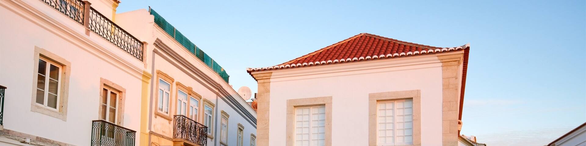 A cobblestone street with historic buildings, a market sign, and a pigeon on the ground.