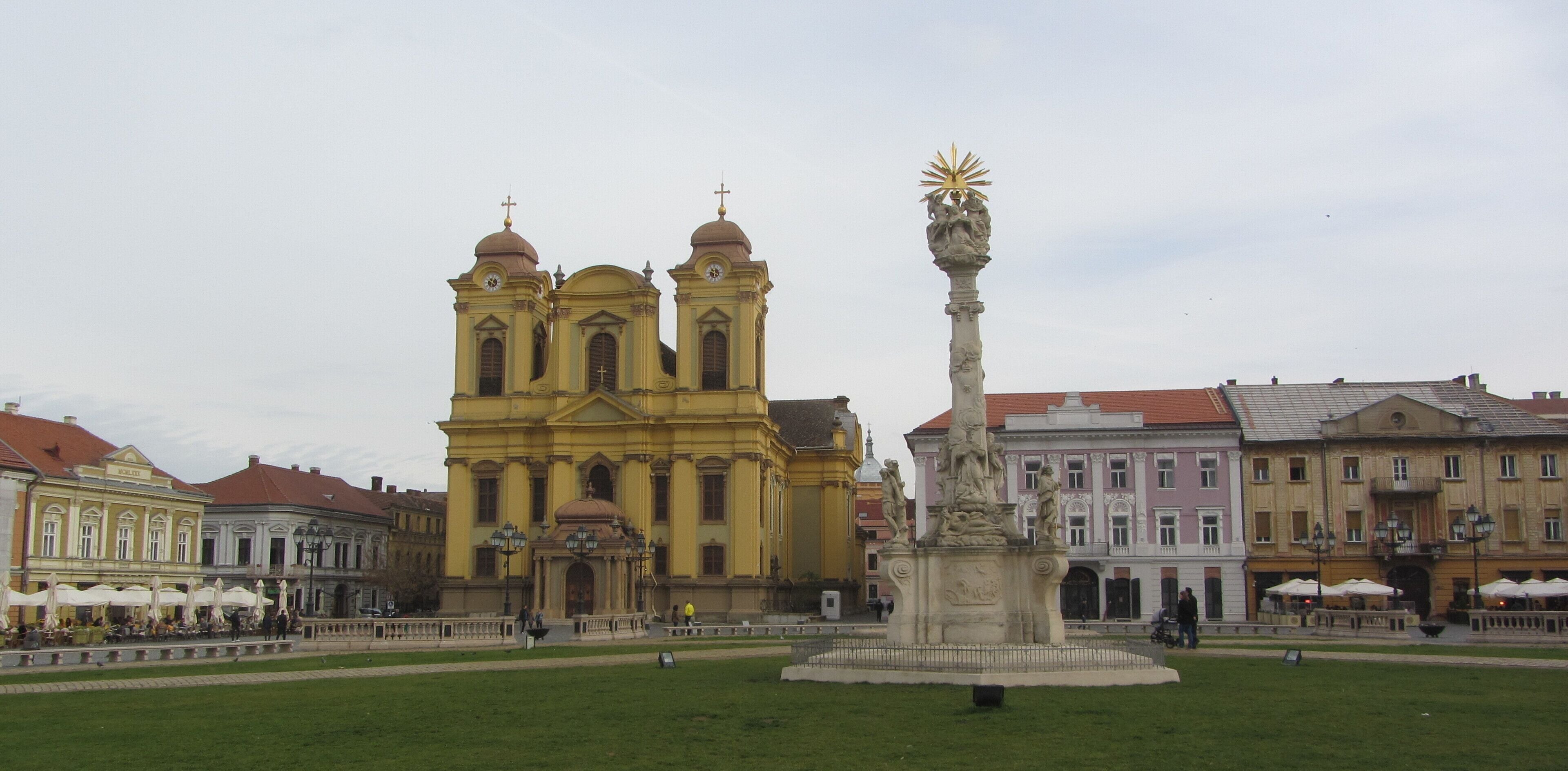Eine gelbe Kirche mit zwei Türmen, einer Statue und umliegenden Gebäuden.