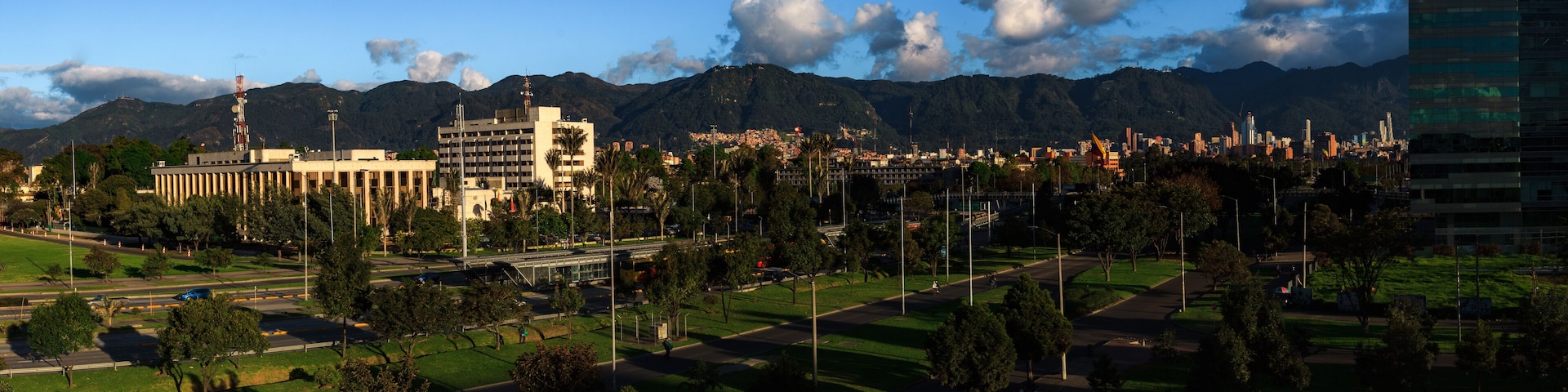 Paisagem urbana com montanhas ao fundo, uma mistura de edifícios modernos e antigos, e uma área verde de parque.