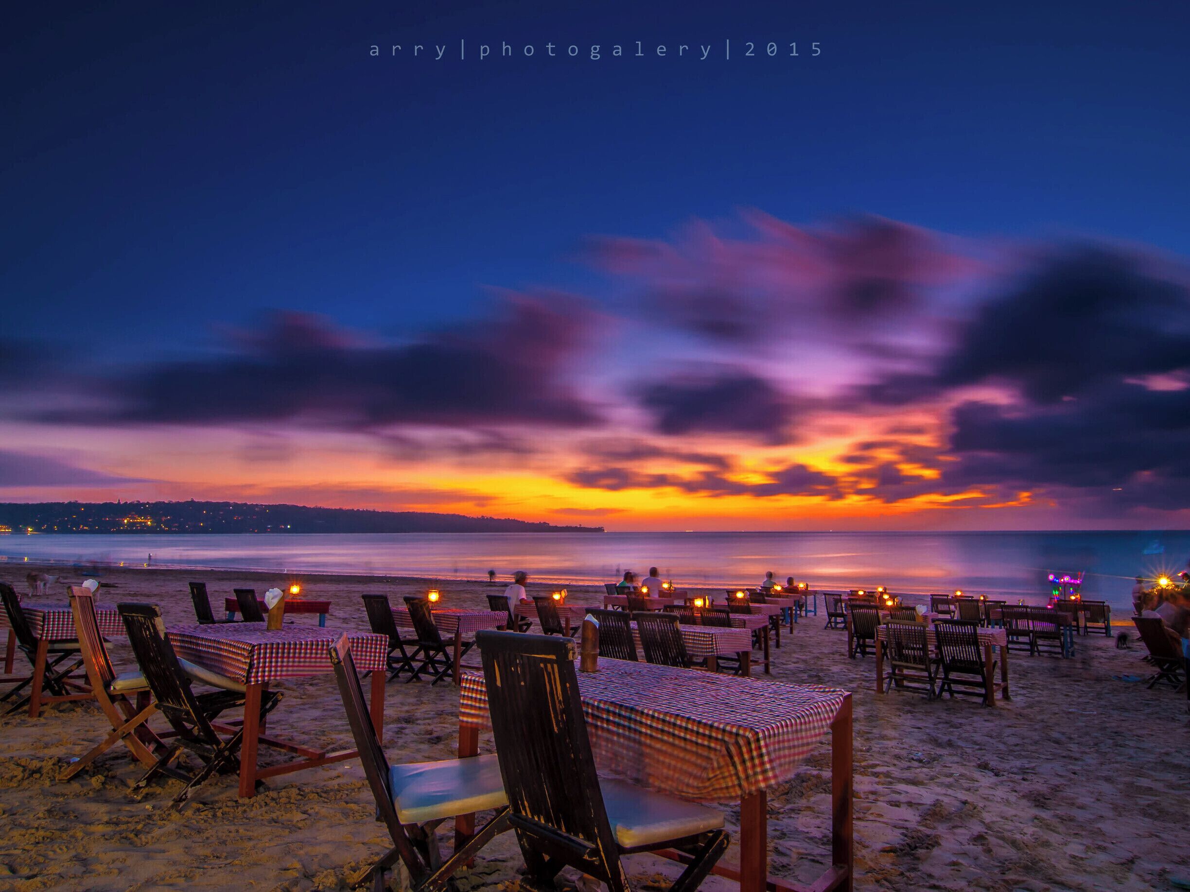 A beach at sunset with tables and chairs set up for dining.