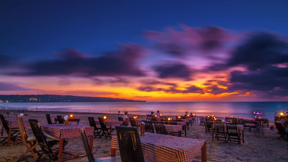 A beach at sunset with tables and chairs set up for dining.