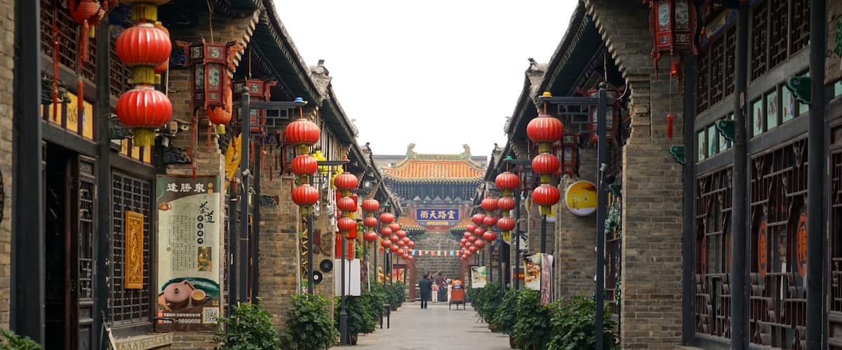 A traditional Chinese alleyway with red lanterns, tiled roofs, and potted plants.