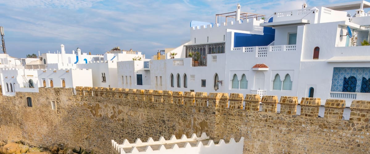 View of the historic stone ramparts and white-washed buildings of the Asilah medina overlooking the rocky Atlantic coastline in Asilah, Tangier-Tetouan-Al Ho, Morocco.