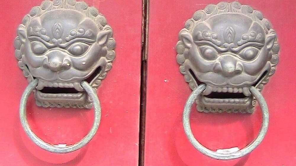 A pair of ornate metal door handles with circular rings on a red door.