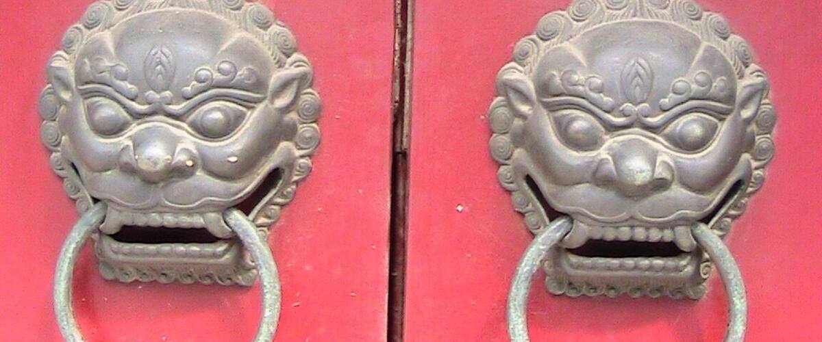 A pair of ornate metal door handles with circular rings on a red door.