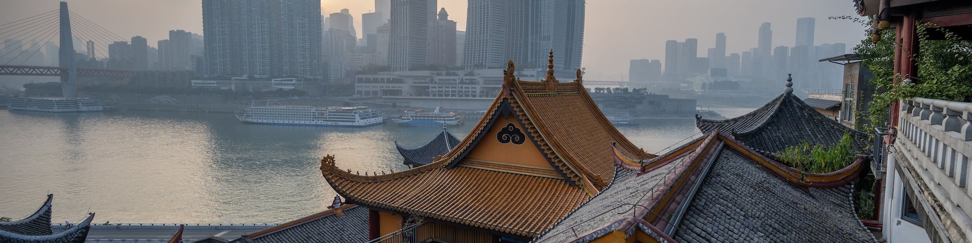 A traditional Chinese roof with a river and modern skyscrapers in the background.