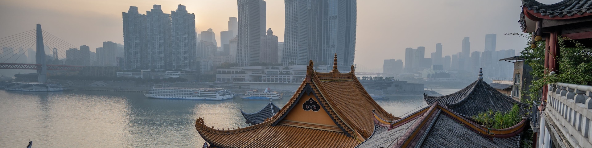 Telhado tradicional chinês com um rio e arranha-céus modernos ao fundo.