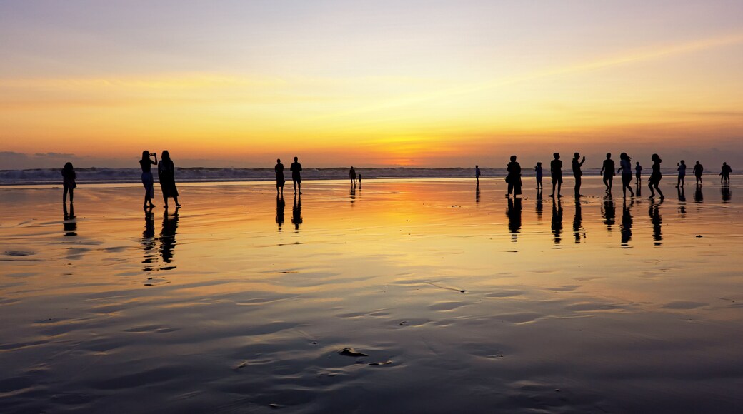 Silhouettes of people enjoying sunset in Seminyak beach, Kuta, Bali, Indonesia.