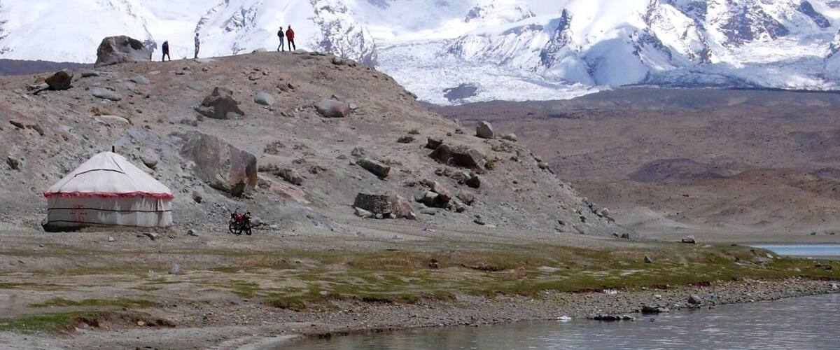 A snowy mountain range, a small yurt, and a calm lake.