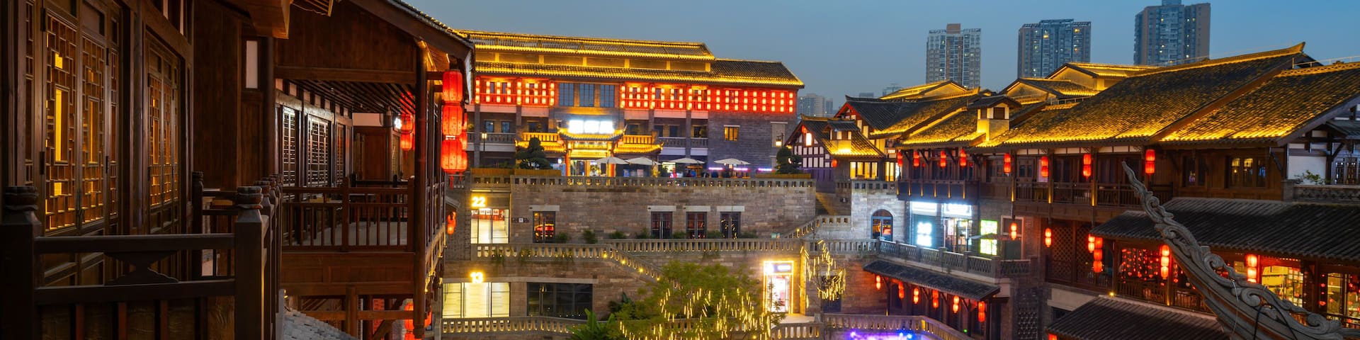 A traditional courtyard with wooden buildings, a stone bridge, and a river.