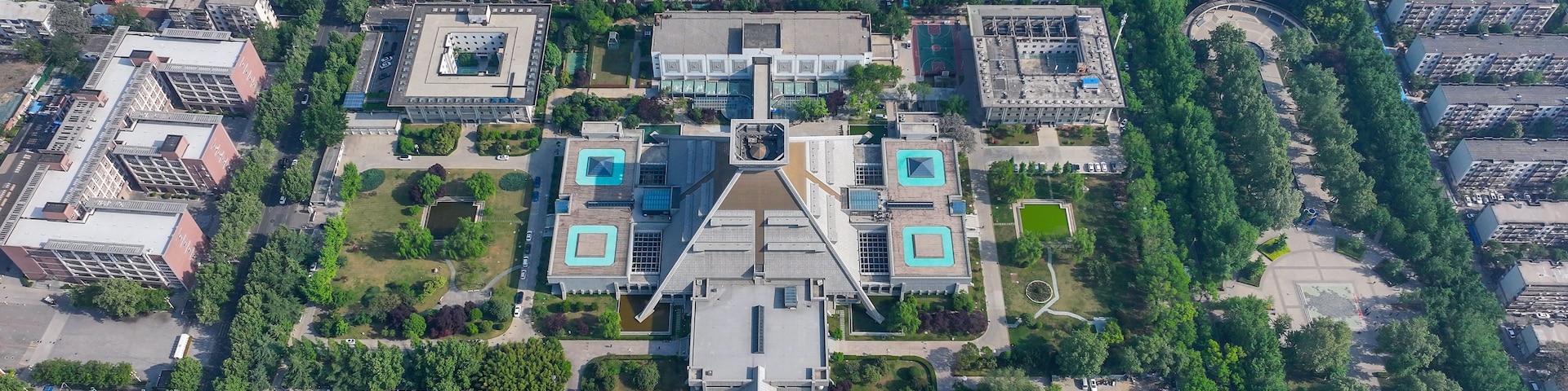 Vista aérea de uma área urbana densamente povoada, com edifícios residenciais altos, uma praça central com uma fonte e um campo esportivo.