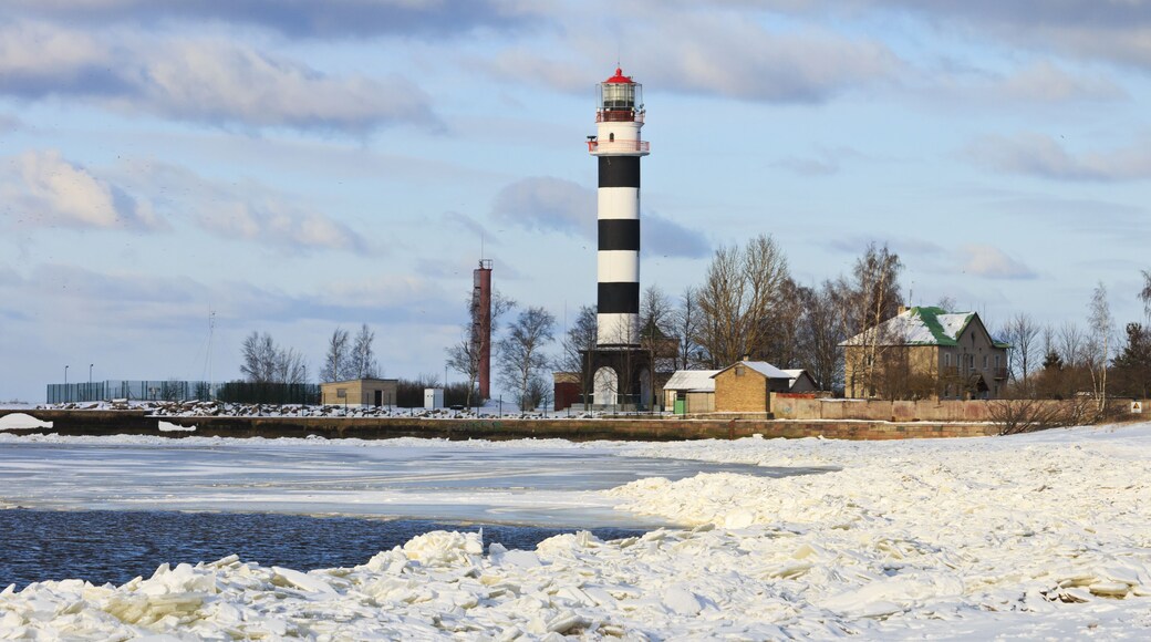 A lighthouse with a black and white striped tower, surrounded by snow-covered ground and a frozen body of water.