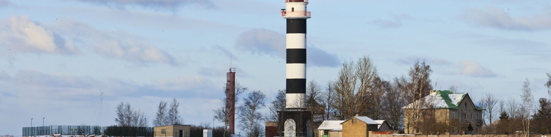 A lighthouse with a black and white striped tower, surrounded by snow-covered ground and a frozen body of water.