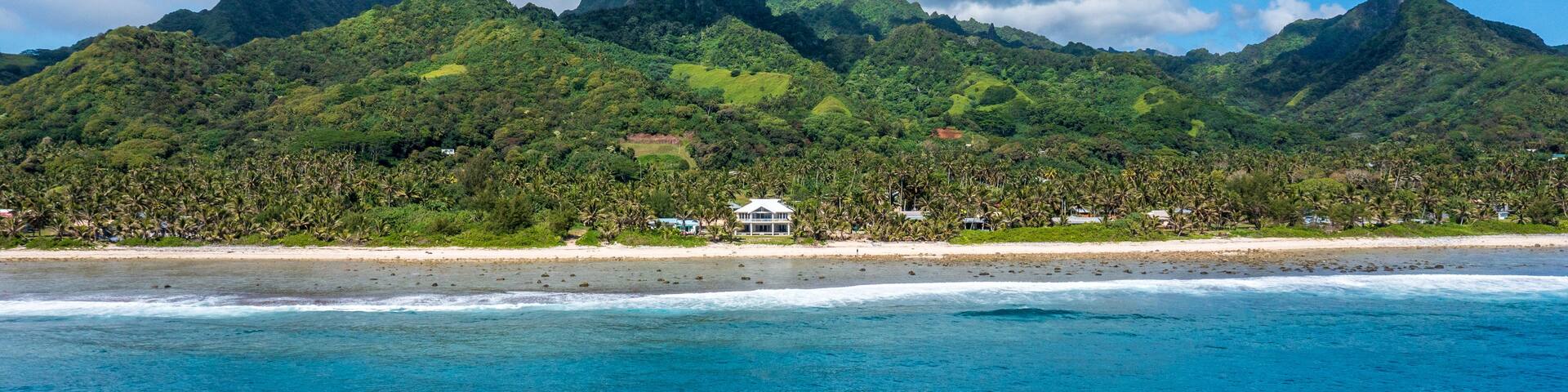 A coastal landscape with a beach, a mountain range, and a clear blue sea.