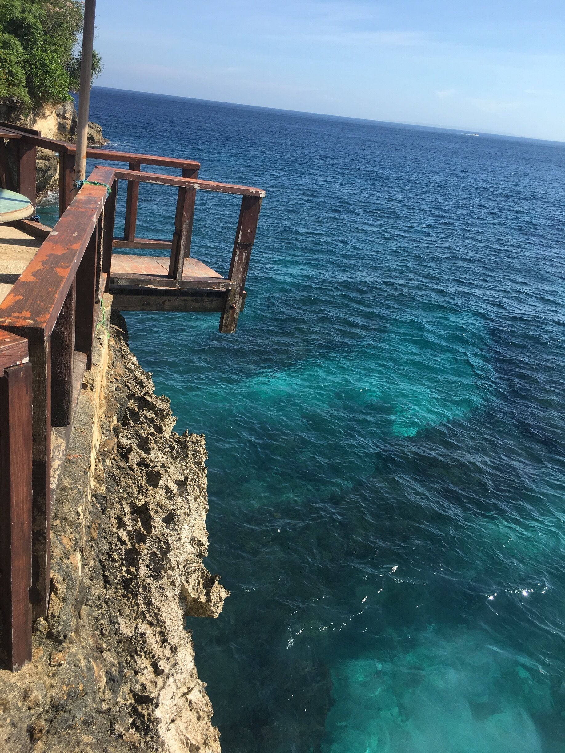 Un muelle de madera que se extiende sobre aguas azul turquesa, con una costa rocosa al fondo.