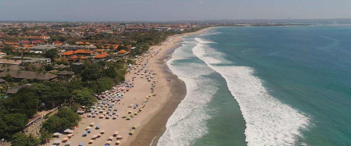 An aerial view of a beach with a row of houses and umbrellas along the shoreline.