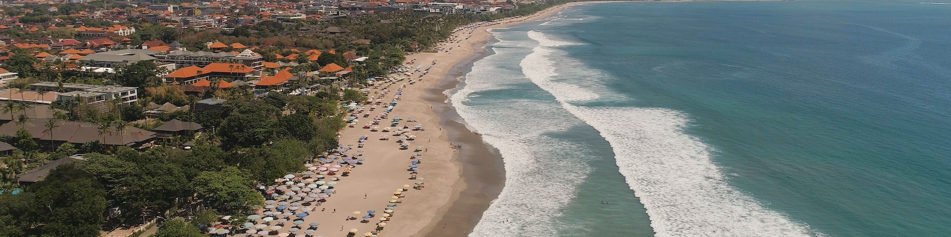 An aerial view of a beach with a row of houses and umbrellas along the shoreline.