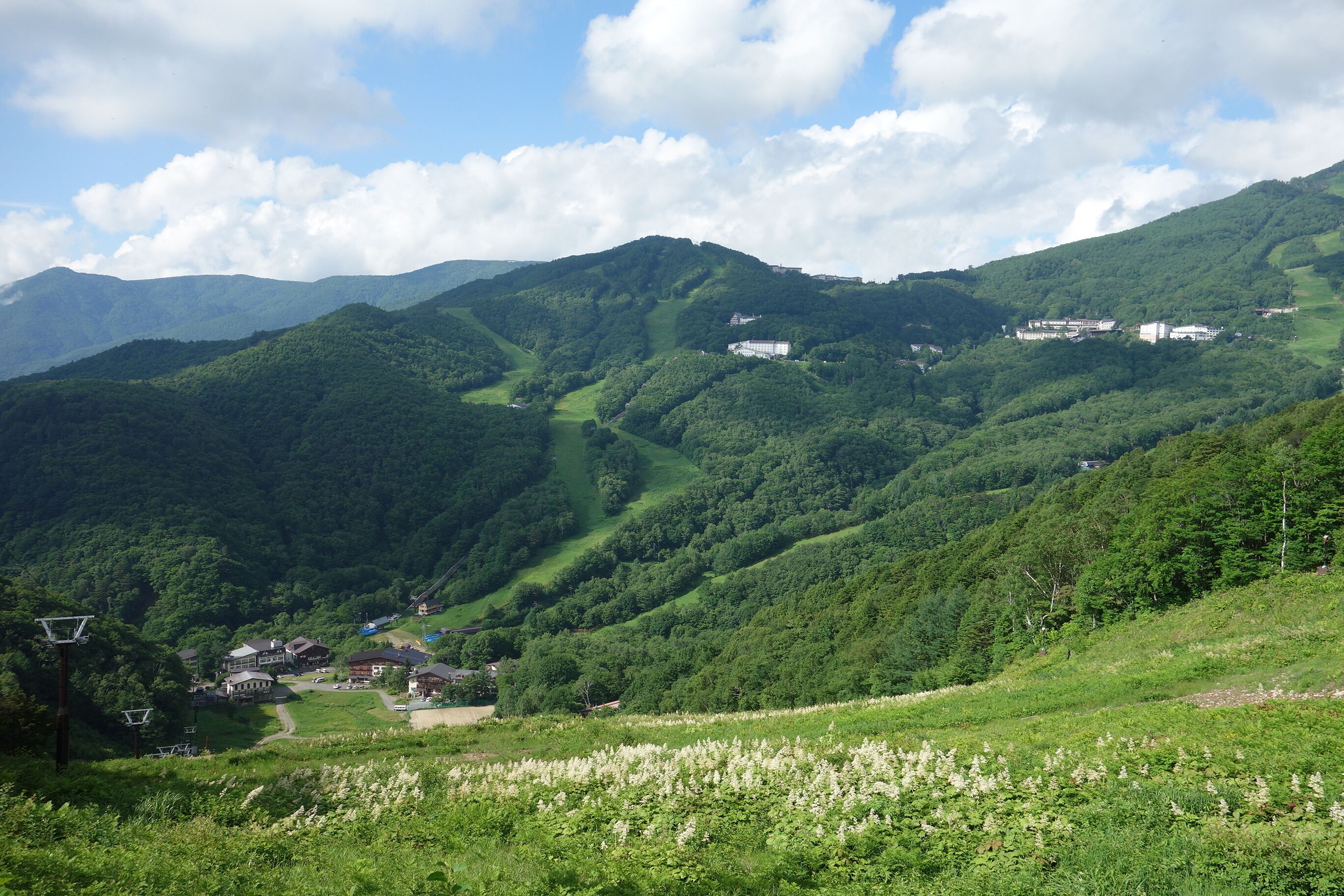 A mountainous landscape with lush greenery, a winding road, and scattered buildings.