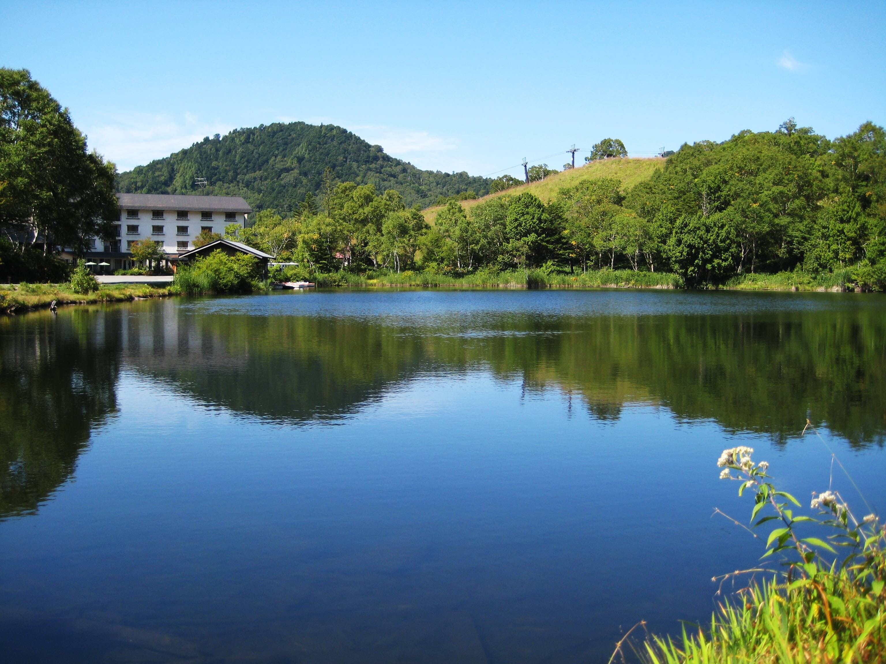A calm lake with a building and trees in the background.