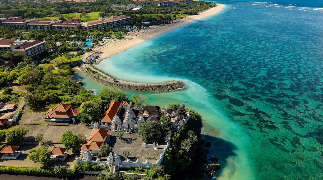Lush tropical coastline featuring cliffside temple, sandy beach and luxury resort hotels