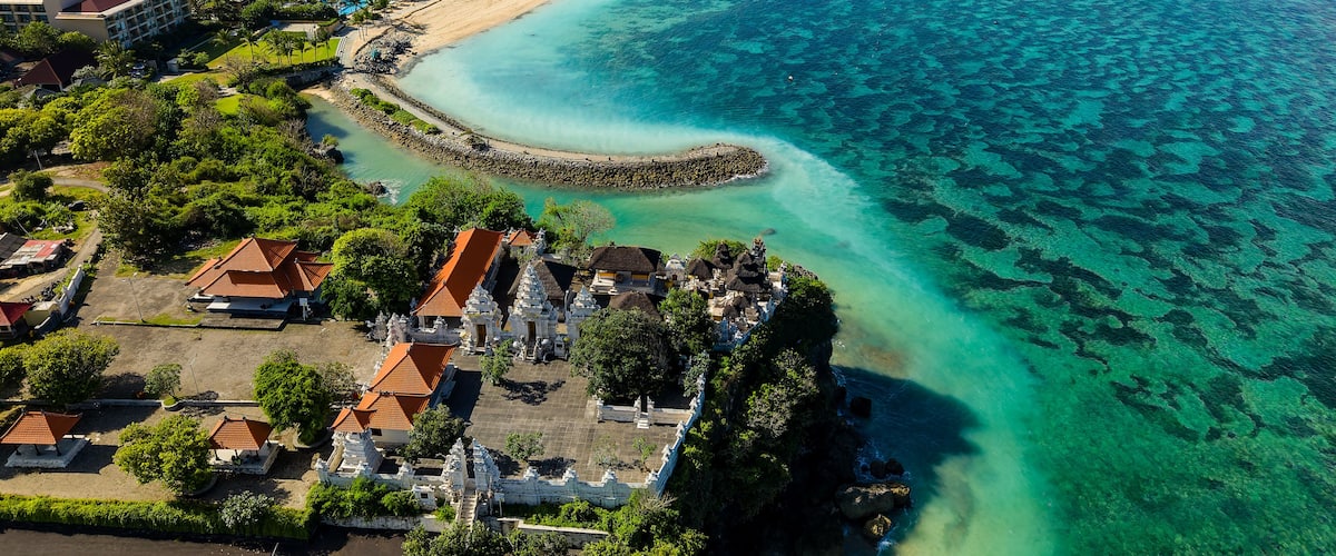 Lush tropical coastline featuring cliffside temple, sandy beach and luxury resort hotels