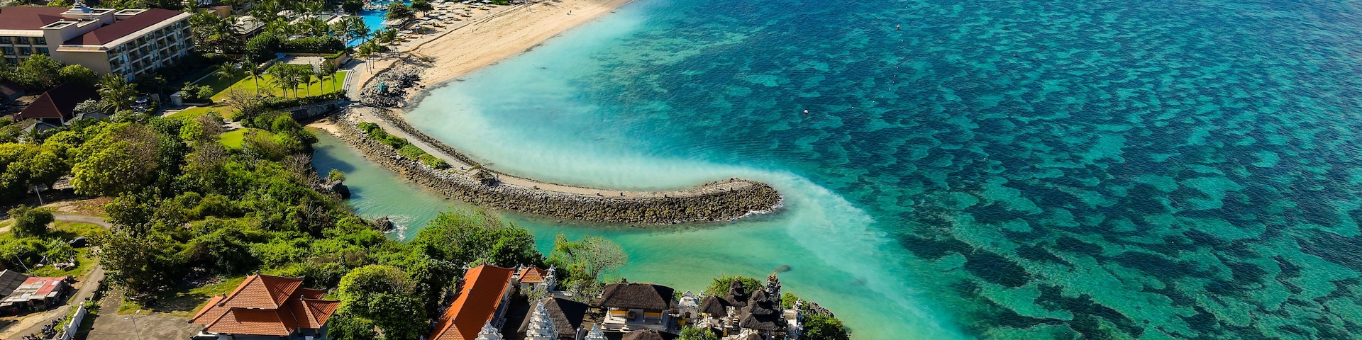 Ein Küstenort mit Strand, klarem türkisblauem Wasser und üppiger Vegetation.