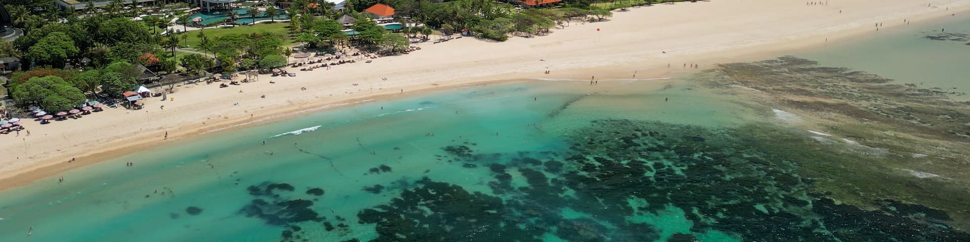 A coastal resort with a sandy beach, clear turquoise waters, and red-roofed buildings.