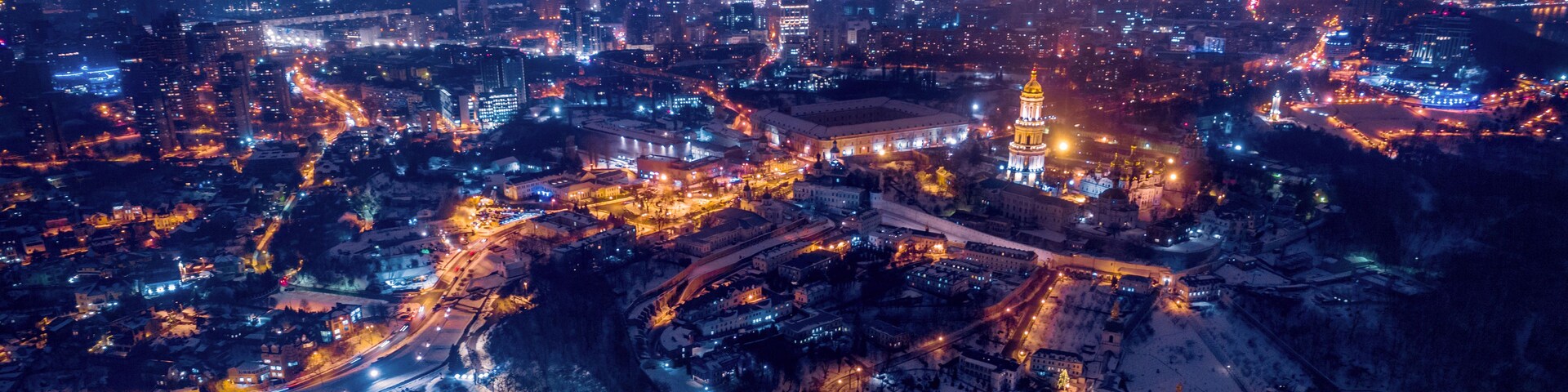 Un paisaje urbano nocturno con edificios iluminados y una torre destacada.
