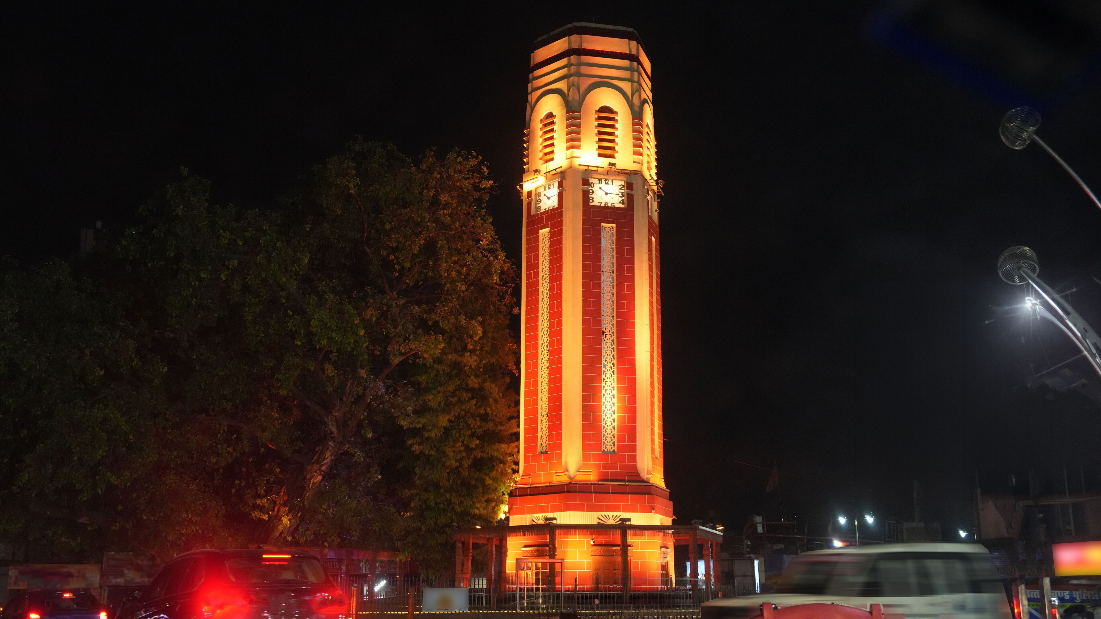 Night view of the illuminated Dehradun Clock Tower in Uttarakhand, India, glowing with warm architectural lighting against a dark sky. A landmark city scene featuring historic tower architecture