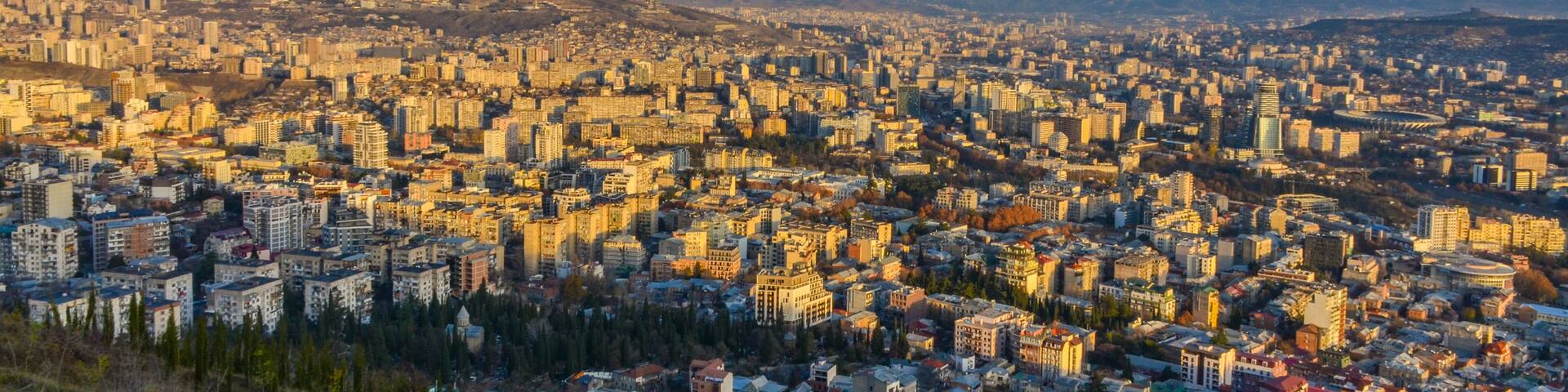 A panoramic view of a city with a dense urban landscape, a clear sky, and distant mountains.