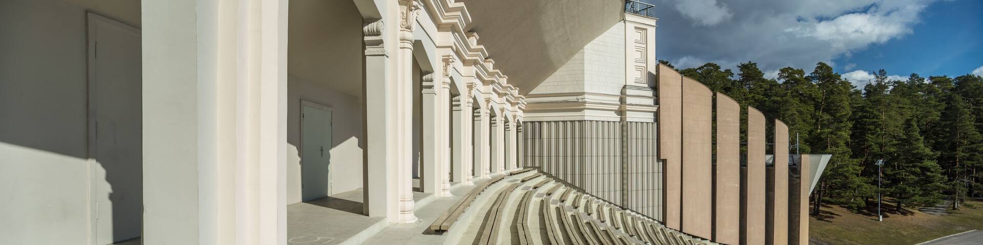 A grand architectural structure with columns and a sloped roof, surrounded by a forested area.