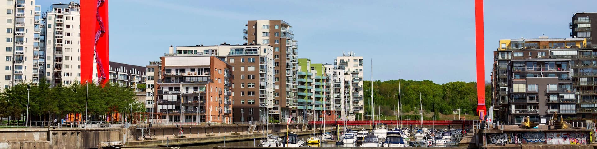 A red arch with 'ERIKSBERG' written on it, a marina with boats, and modern buildings in the background.