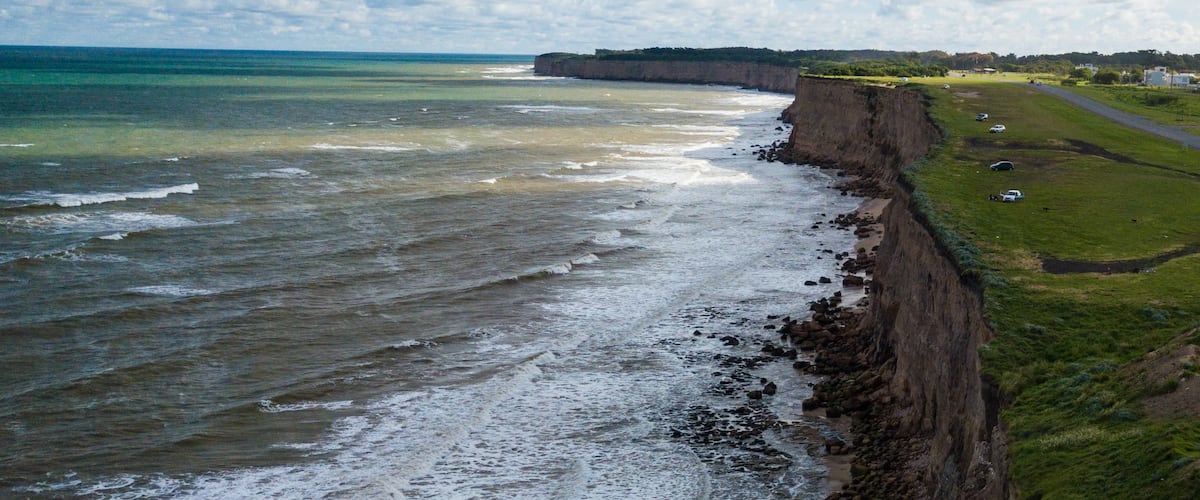 Un paysage côtier avec des falaises, une zone herbeuse et une route.