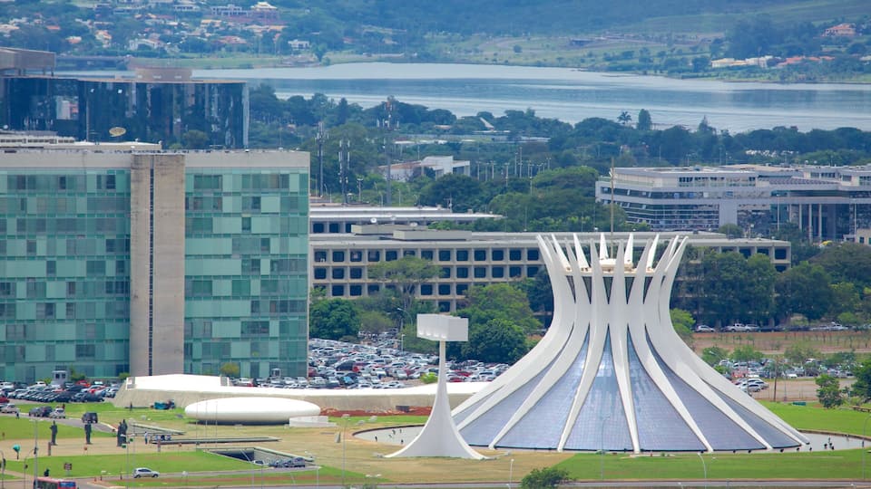 A modern building with a unique curved roof, surrounded by a parking lot and a body of water in the background.