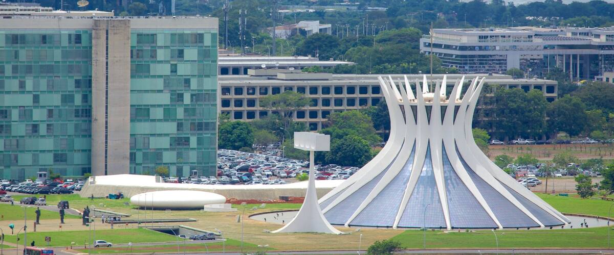 A modern building with a unique curved roof, surrounded by a parking lot and a body of water in the background.