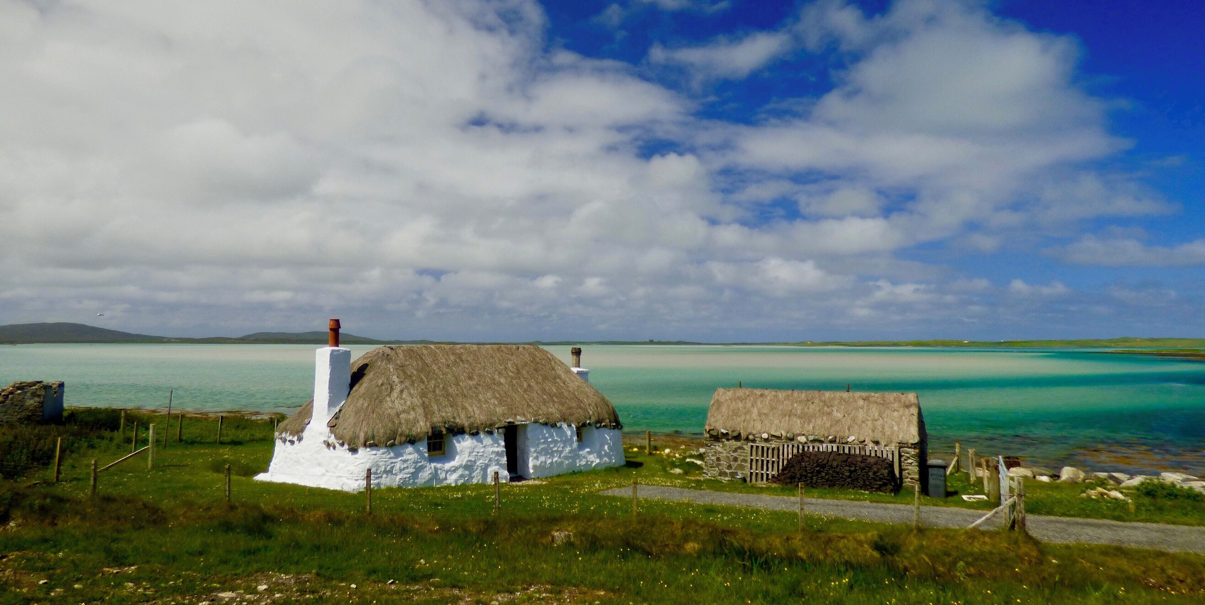 The restored Cottages of Struan near Malacleit are a beautiful example of traditional life on the Isle of North Uist, the clear waters of the bay shown the underlying white sands and the Isle of Vallay in the distance. 