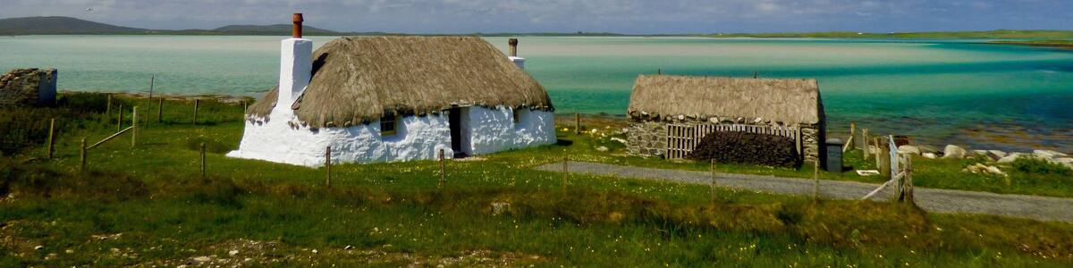 The restored Cottages of Struan near Malacleit are a beautiful example of traditional life on the Isle of North Uist, the clear waters of the bay shown the underlying white sands and the Isle of Vallay in the distance.