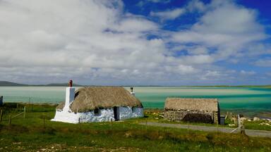 A thatched-roof house near a turquoise sea with a clear sky.